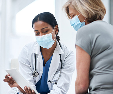 Diagnostic Safety - Doctor and patient, in masks, reviewing file on a tablet