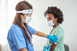 A medical professional provides a vaccination for a young woman of color
