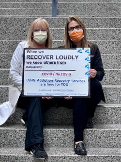 Paige Roth and Holly Maddox hold a sign that reads 'When we recover loudly, we keep others from dying quietly. COVID/NO COVID - LVHN Addiction Recovery Services are here for you.'